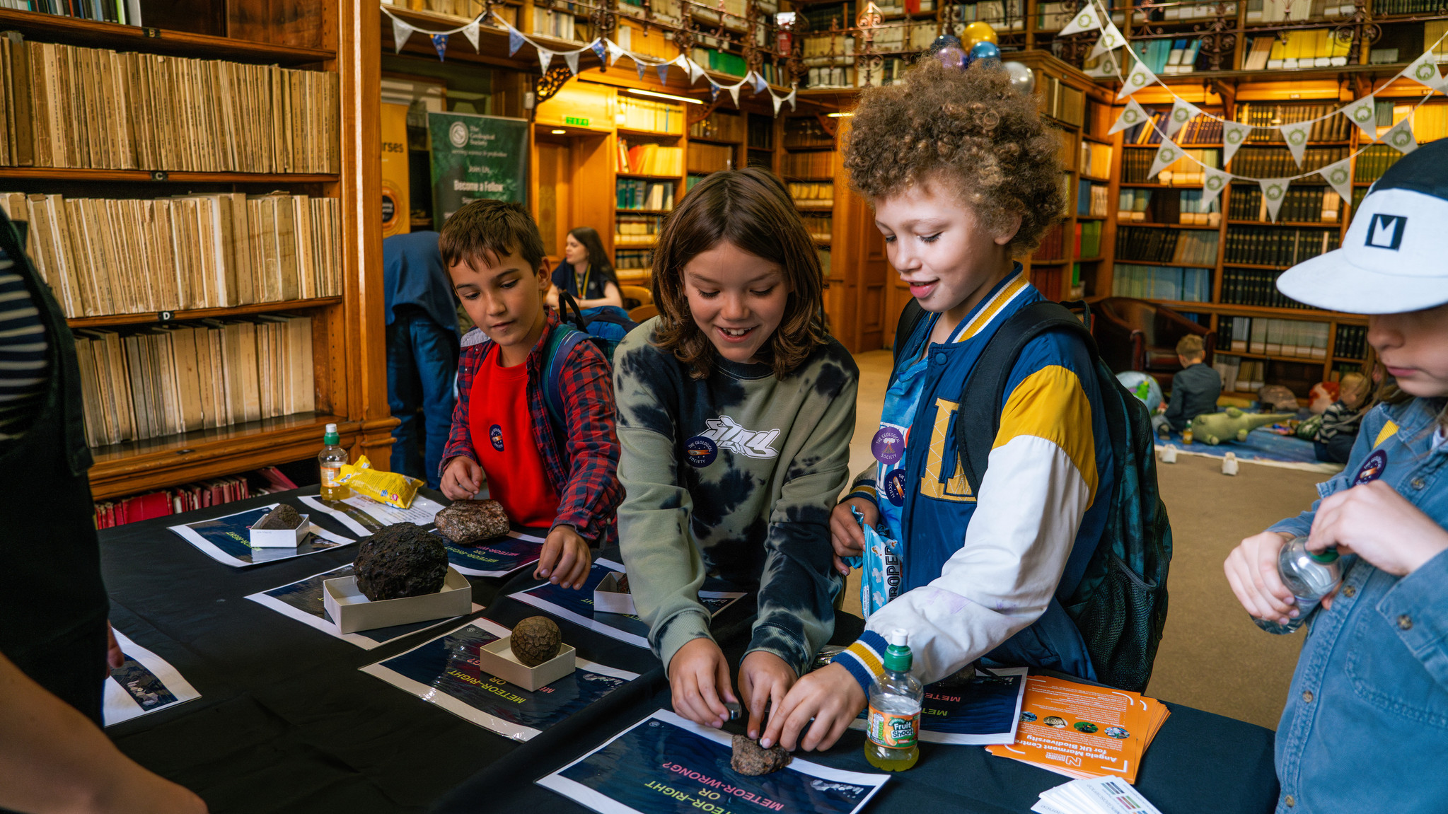 three young boys smiling whilst looking at a display of meteorites on a table