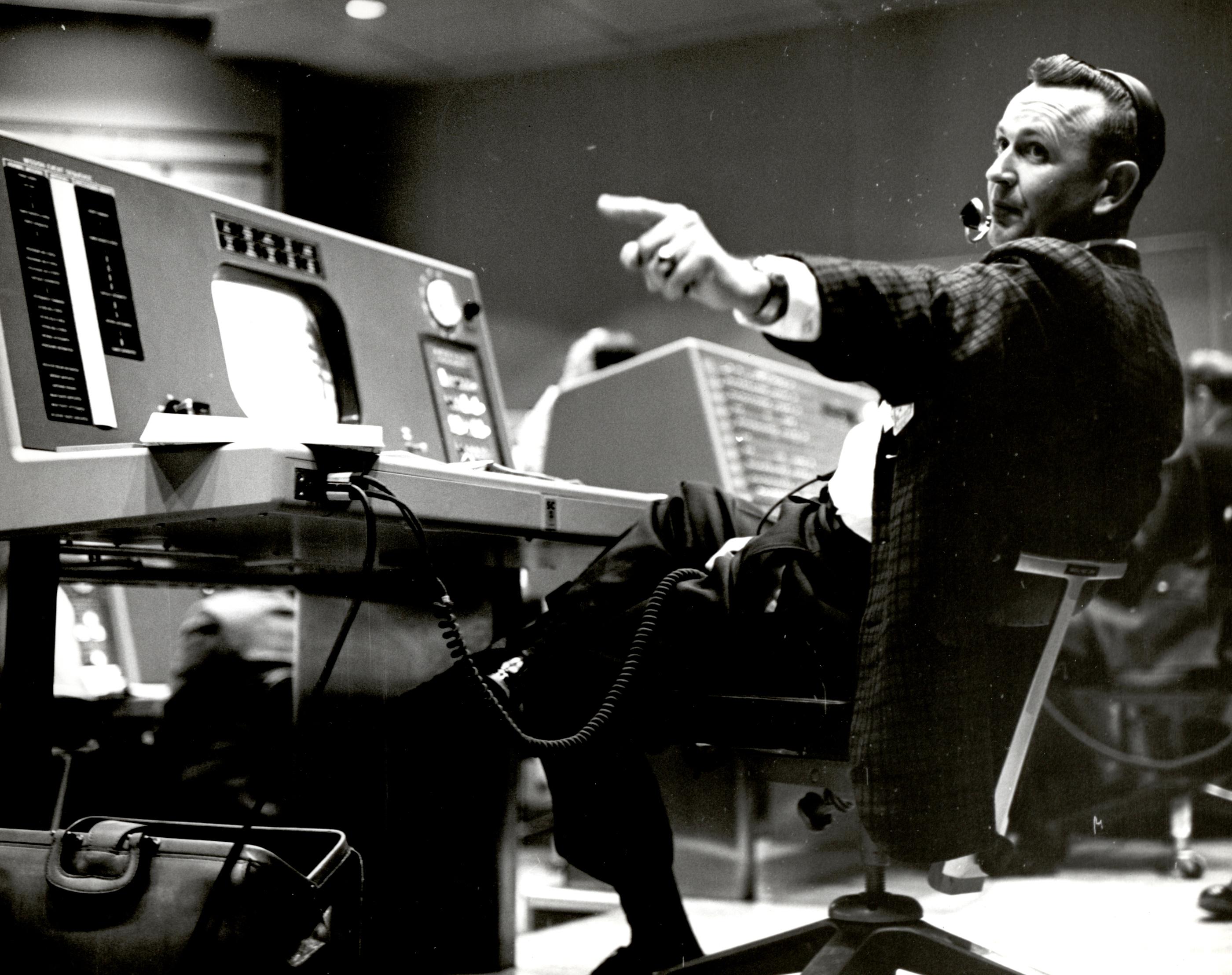 Flight Director Chris Kraft at his console at the Mercury Control Center pointing off to the left beyond the shot of the photo. Black and White Image.