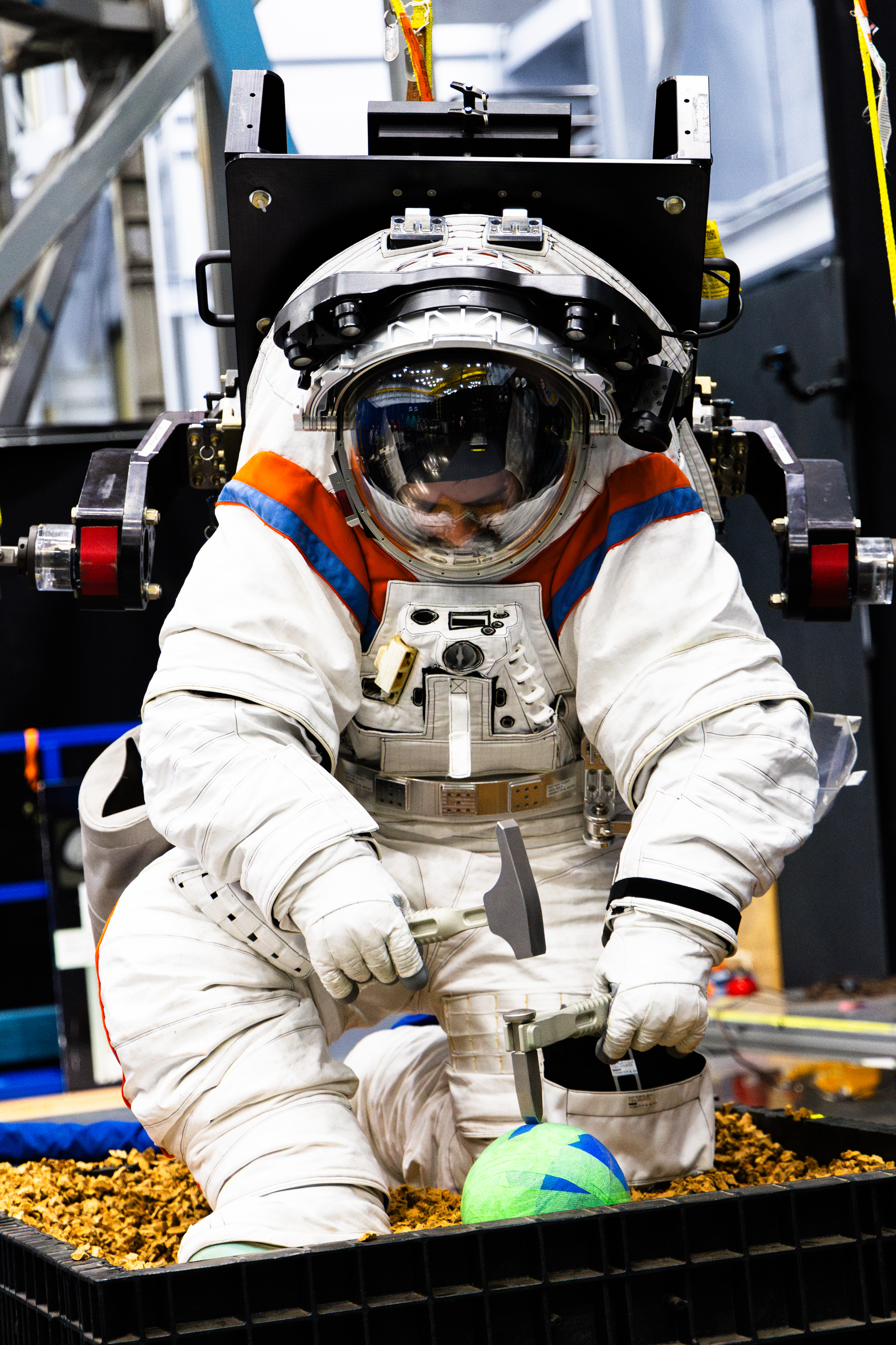 An Axiom Space engineer uses a hammer and chisel to chip off simulated lunar rocks while wearing the AxEMU (Axiom Extravehicular Mobility Unit) spa...