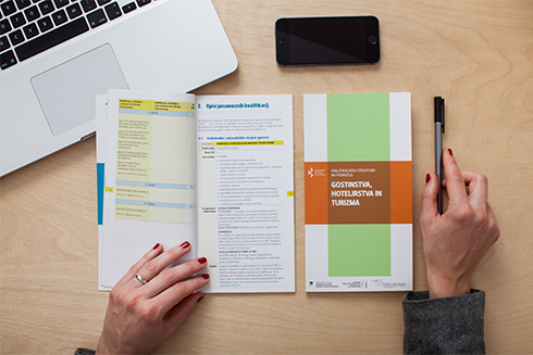 A person is reading a SQF brochure on a desk next to a laptop. 
