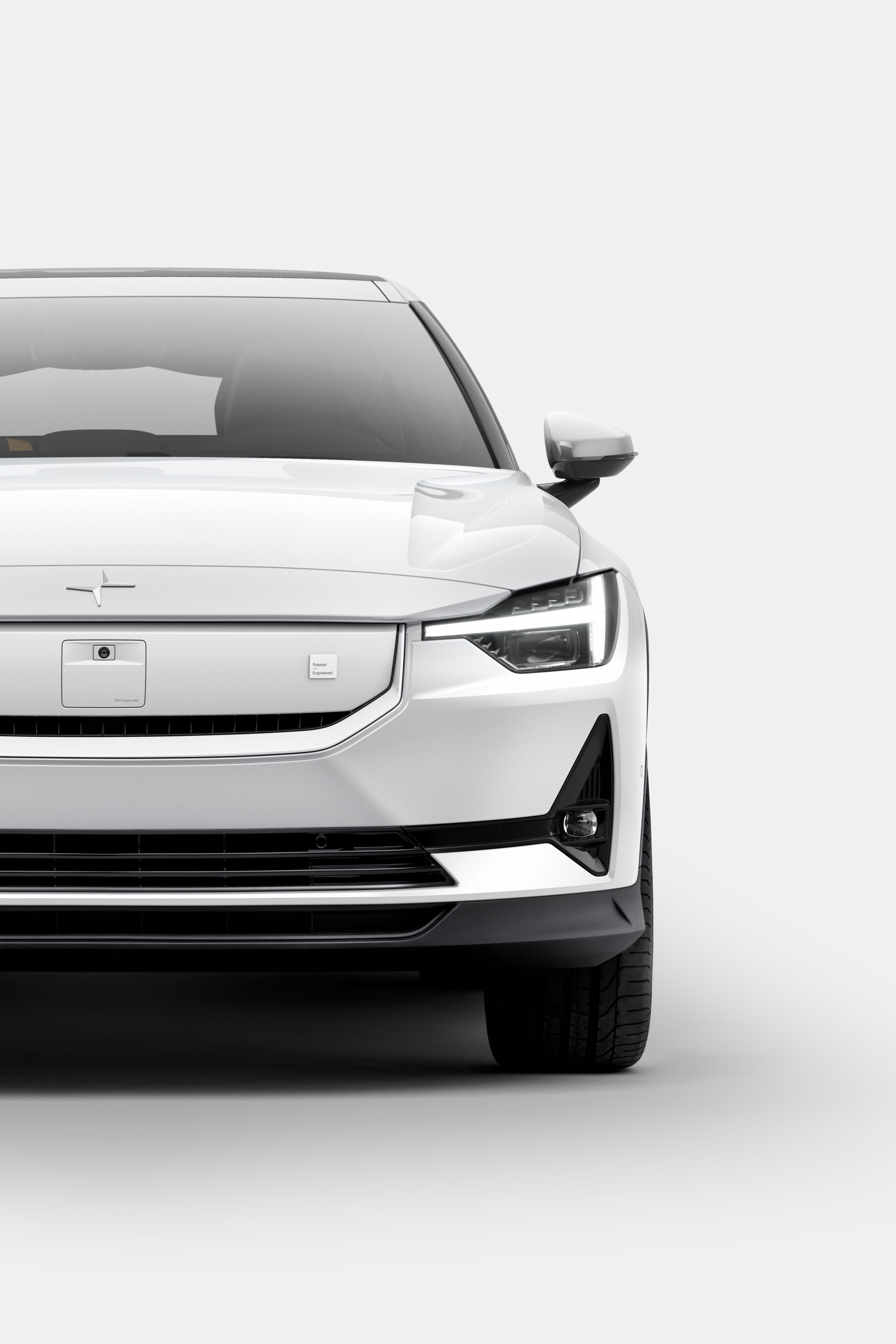 Front view of a white Polestar car with headlights on against a plain background.