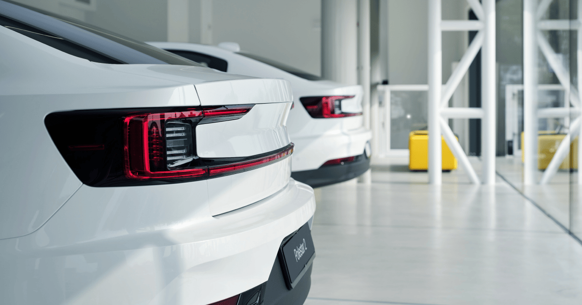 Two white Polestar cars parked indoors with visible rear lights and a yellow object in the background.v